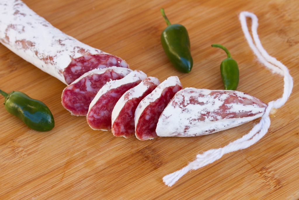 Spanish fuet sausages with green peppers on wooden table